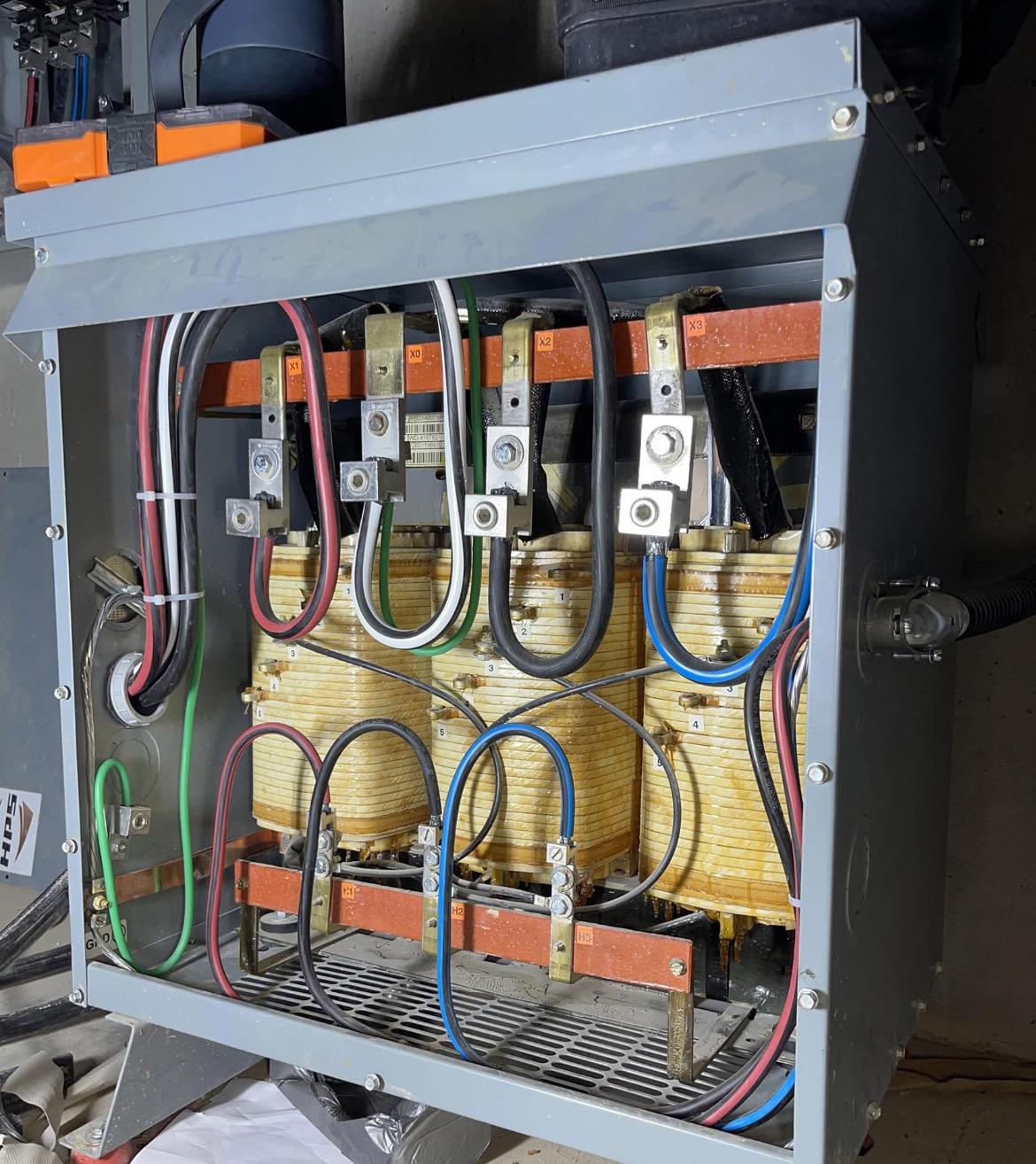 Open dry-type transformer enclosure showing three windings with primary and secondary busbars landed and labelled