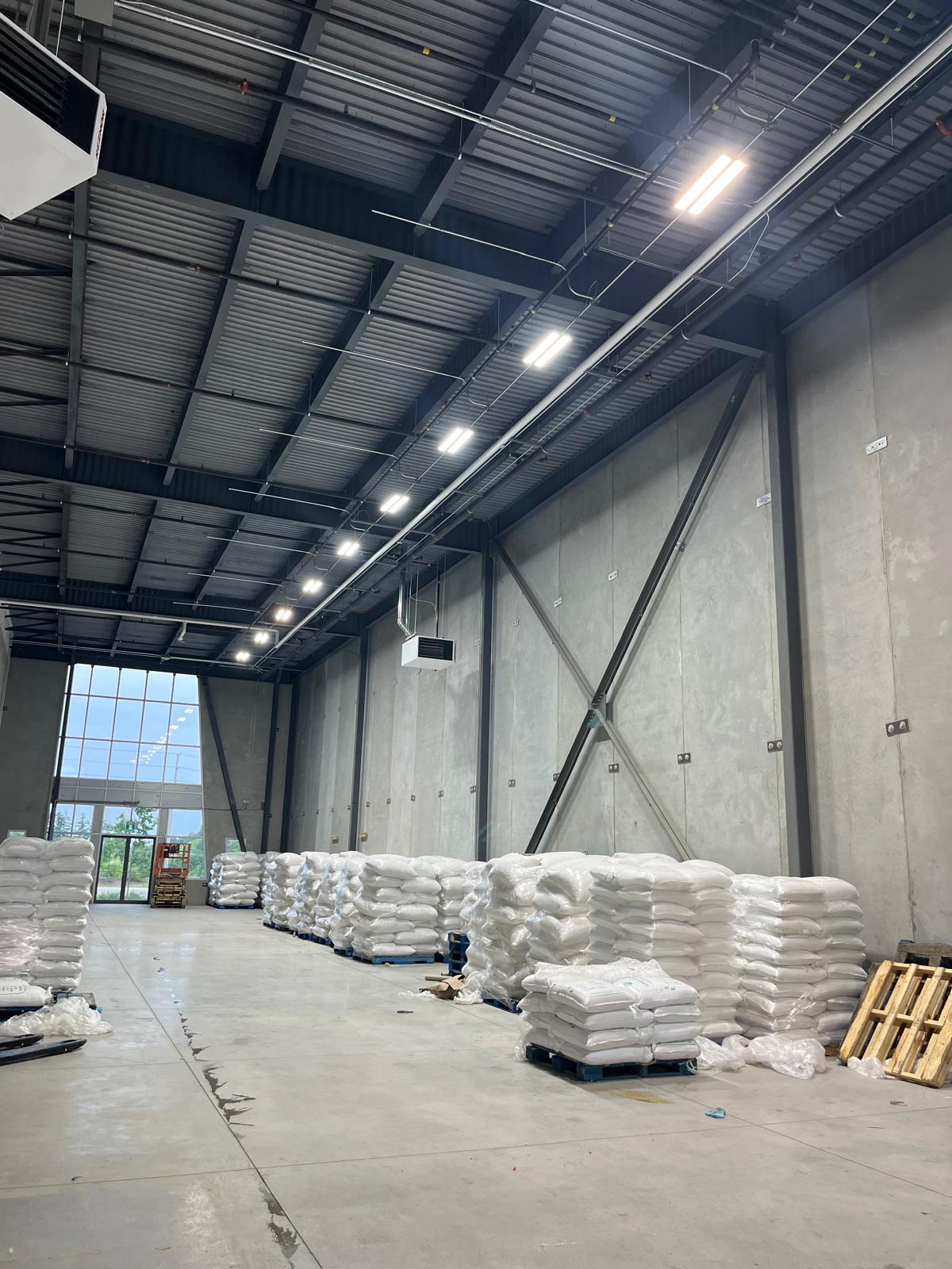 A continuous run of linear LED fixtures and conduit following a precast concrete warehouse wall